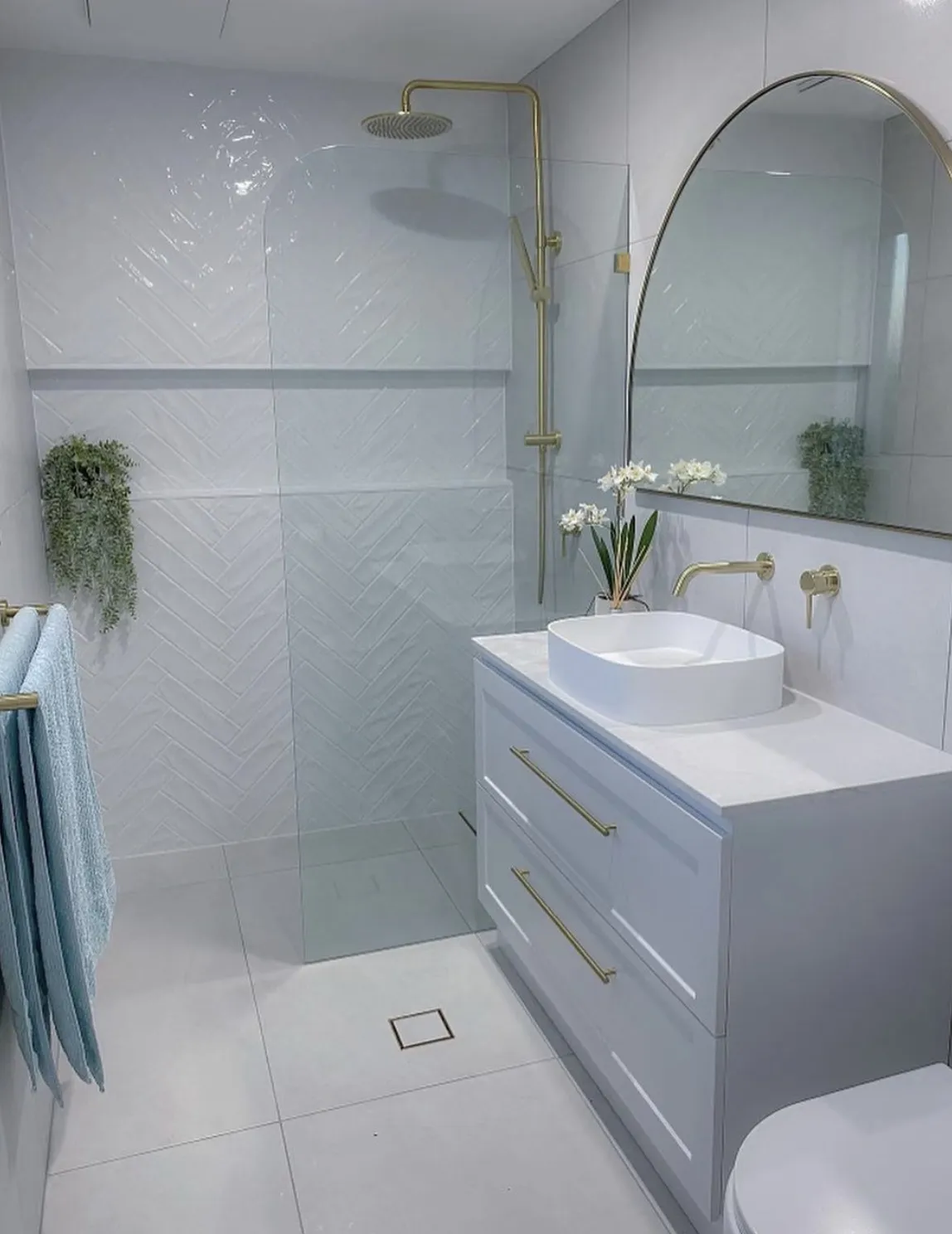 JL Coastal Projects completed a modern white bathroom renovation with gold fixtures and a walk-in shower, creating a luxurious and elegant space.